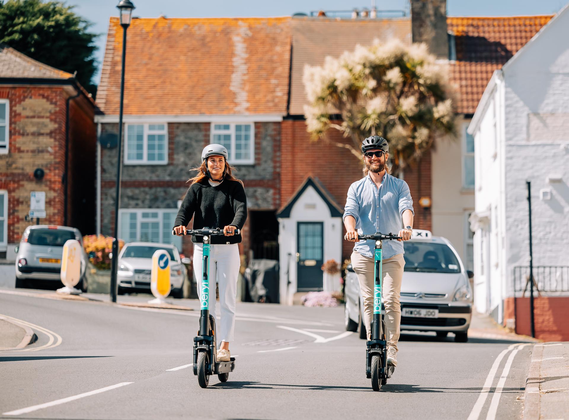 Man and woman wearing helmets and riding Beryl scooters