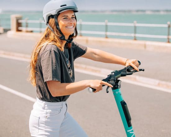 Woman wearing a helmet with a scooter beside the seafront