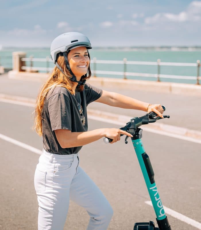 Woman wearing a helmet with a scooter beside the seafront